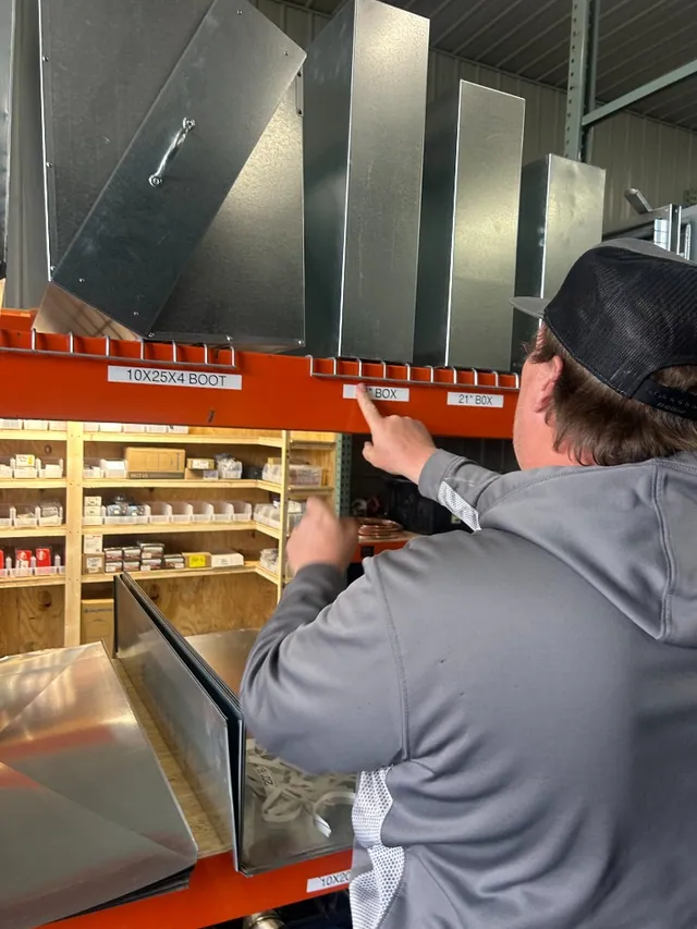 A technician selecting labeled ductwork from stocked warehouse shelving