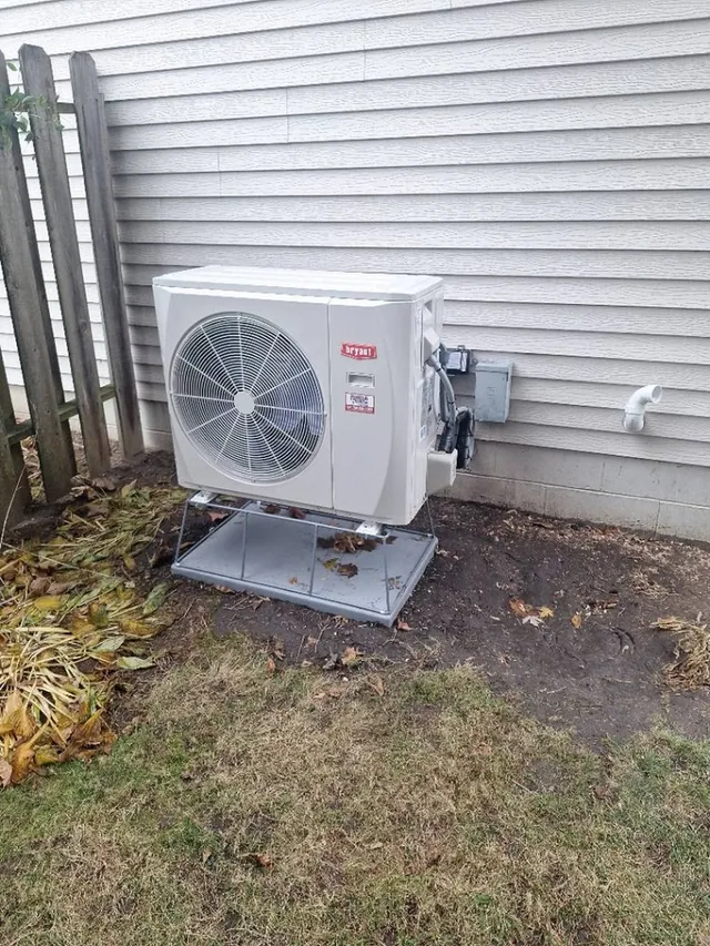 A Bryant outdoor heat pump unit installed on a stand beside a home