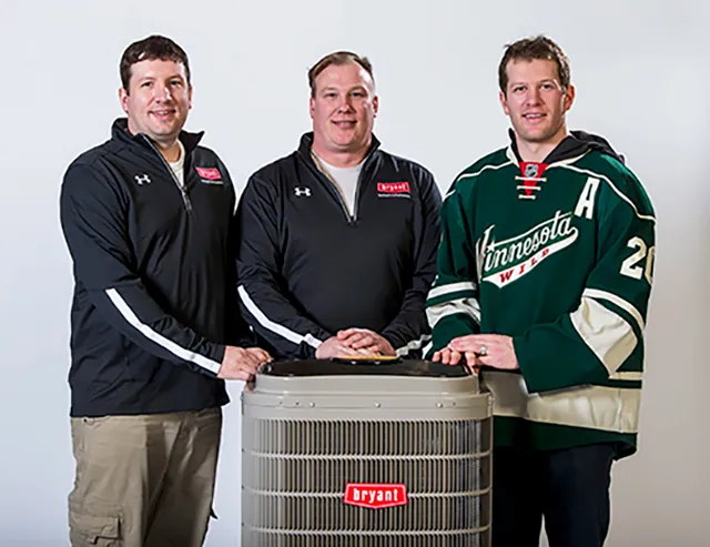 Mankato Heating & Cooling team members standing with a Bryant air conditioner