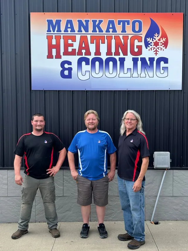 Three Mankato Heating & Cooling technicians in front of the company's building sign